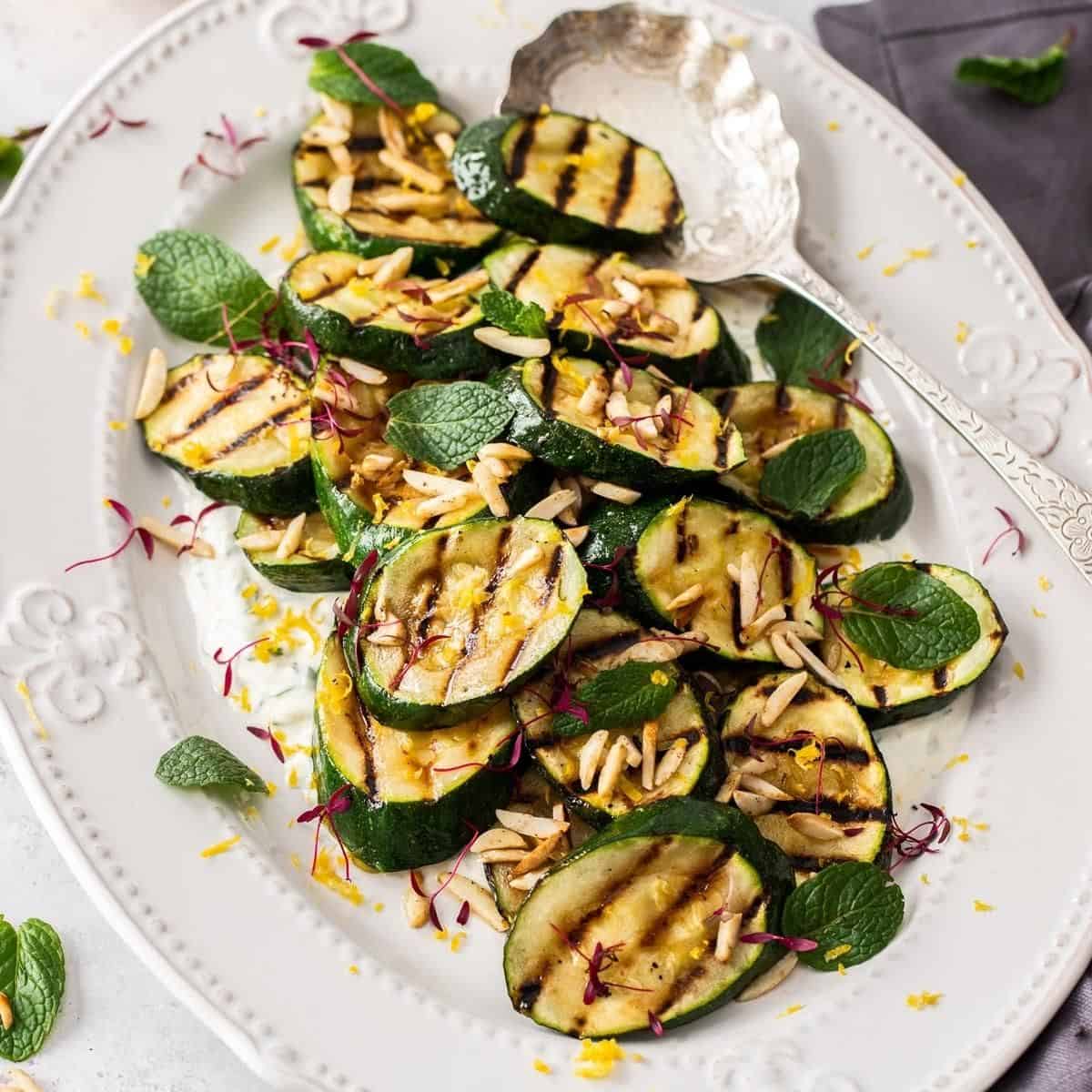 Grilled zucchini with mint, almonds and micro herbs on a white plate