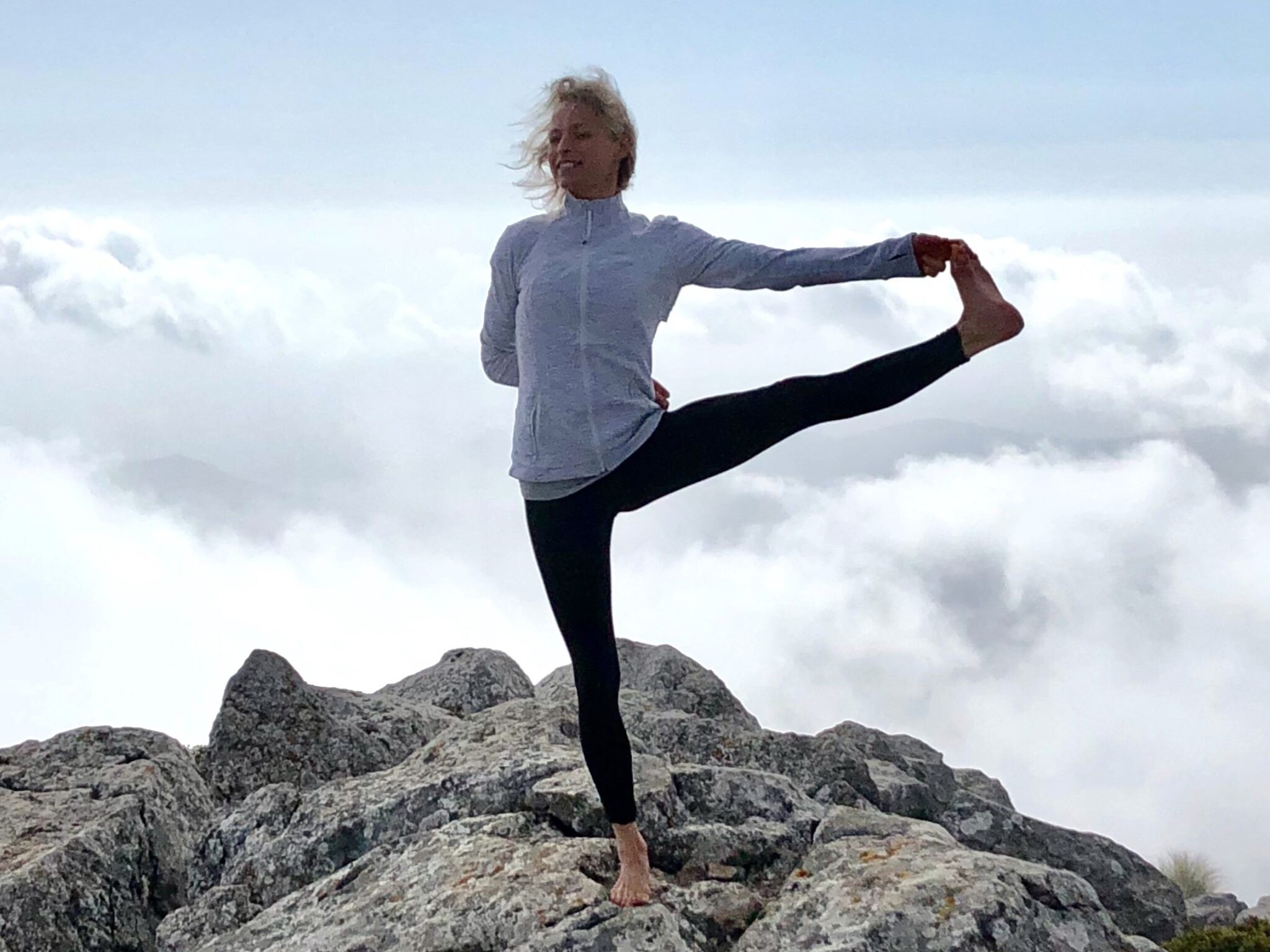 Hanna in a standing balance pose above the clouds, mountain top