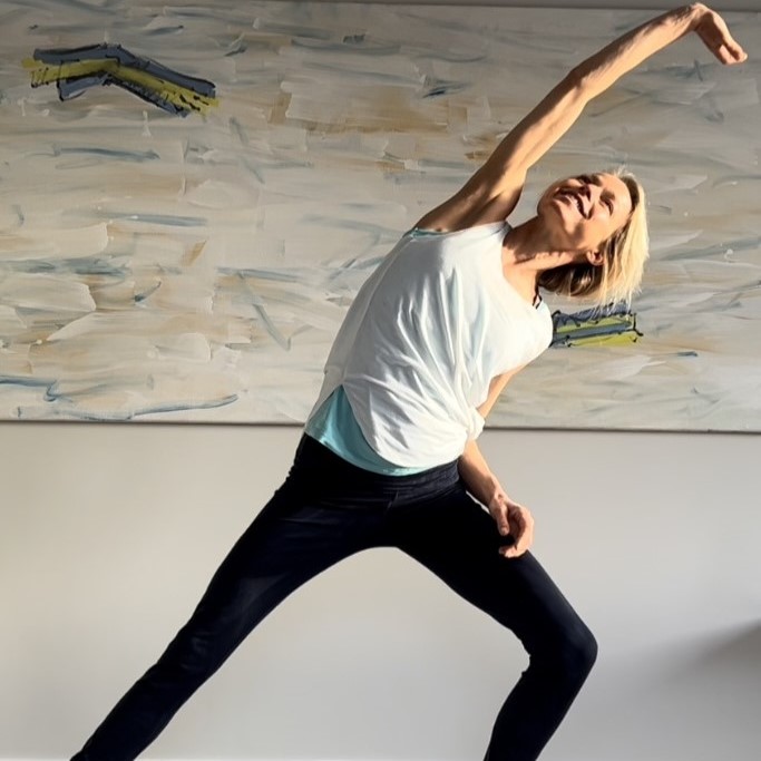 Hanna in an Essentrics side stretch, joyful expression, abstract painting behind her
