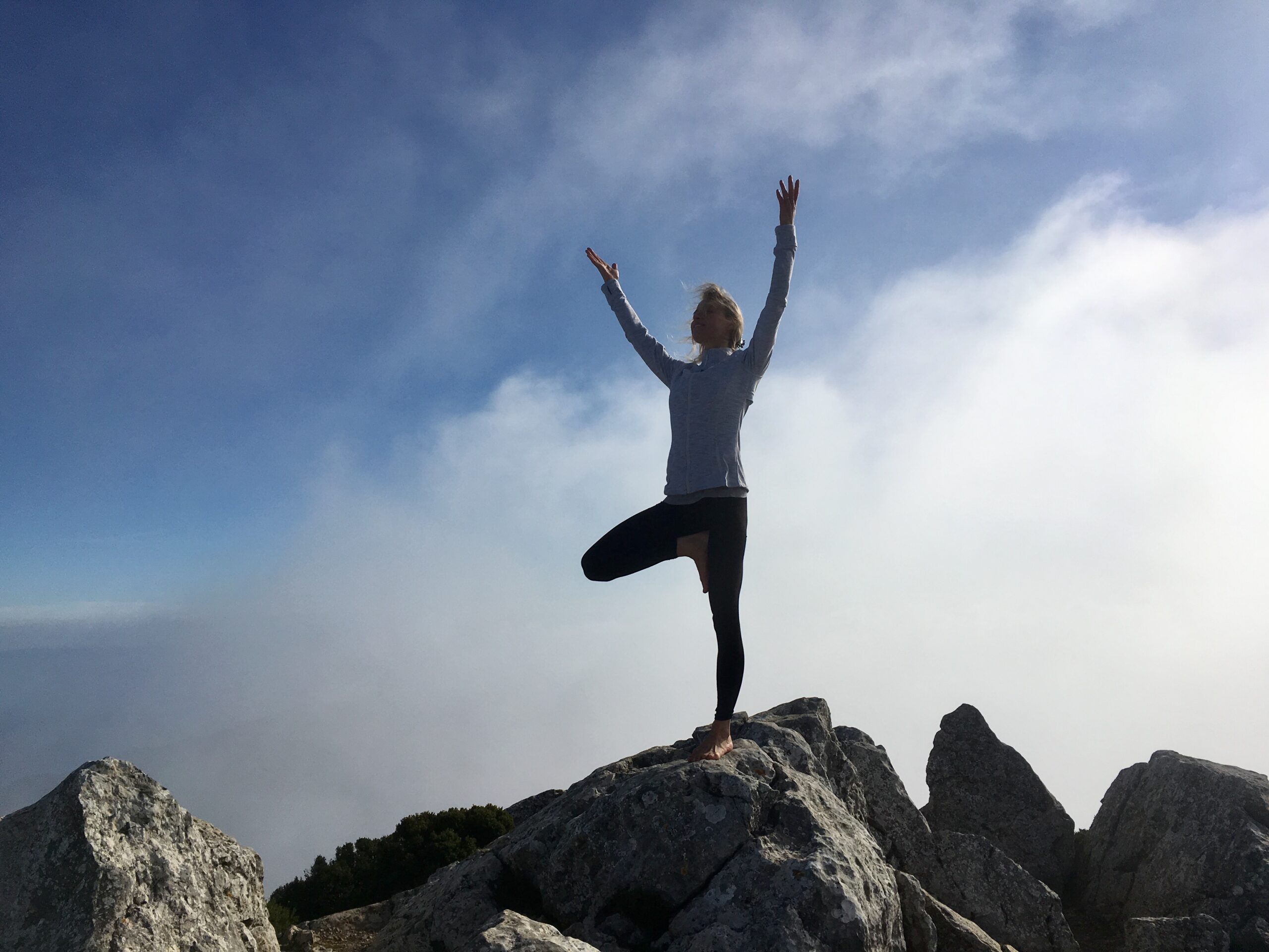 Hanna in tree pose with arms raised, above the clouds in Mallorca